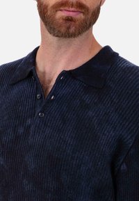 Marineblaues, geripptes Strick-Poloshirt mit klassischem Kragen, Zwei-Knopf-Leiste und dezent strukturierter Optik mit leicht verblasstem Aussehen.