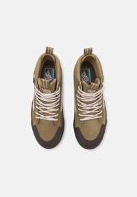 Høye sneakers i olivenfarget semsket skinn og lerret med hvite snorer og en brun gummi såle. Har merkevare og trekkstropper på hælen.