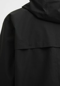 Juodas vandeniui atsparus džemperis su aukštu apykakle, minimalistiniu dizainu ir reguliuojama kapuce, pasižymintis lygiu matinio audinio paviršiumi ir paslėptais siūlais.