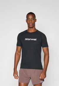 T-shirt de sport noir à manches courtes, en tissu texturé, avec un logo blanc à l'avant. Associé à un short marron.