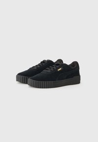Black suede sneakers with a thick rubber sole, featuring a lace-up design, rounded toe, and subtle gold branding. Textured upper with smooth accents.