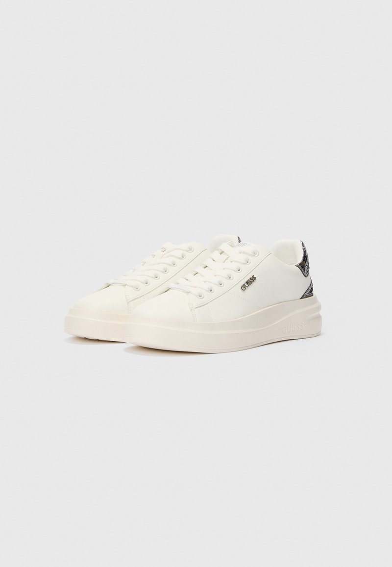 Zapatillas bajas blancas con cordones blancos, suelas gruesas, un logo plateado de Guess en el costado y detalles de talón con un patrón negro.