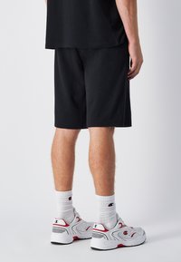 Zwarte katoenen shorts met een ontspannen pasvorm, gecombineerd met witte sportschoenen en kniehoogte witte sokken. Eenvoudig ontwerp zonder opvallende patronen.