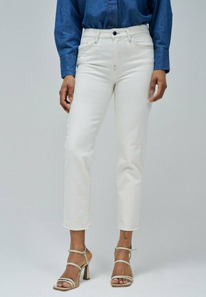 Jeans en denim blanc à coupe slim, jambes droites et détails légèrement déchirés. Associés à des talons beiges à lanières et un haut en denim.