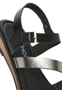 Sandale pour femme en noir et argent métallique avec bride réglable à boucle et semelle rembourrée sur un talon plateforme en bois.