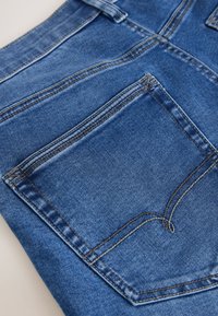 Nahaufnahme von blauem Denimstoff mit Gesäßtasche, orangefarbener Naht und Gürtel-Schlaufe an einer Jeans.