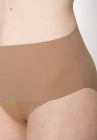 Beige high-waisted brief made from smooth, stretchy fabric. Features a seamless design with a low-cut leg and thin waistband.