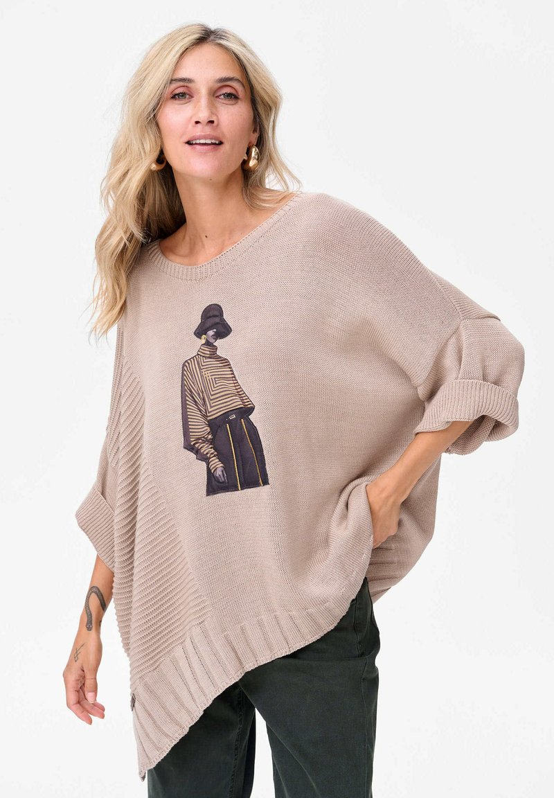 Beżowy sweter z dzianiny o asymetrycznym dolnym wykończeniu, z grafiką postaci w paskowanej bluzce. Żebrowane mankiety i dolny chwyt dodają tekstury.