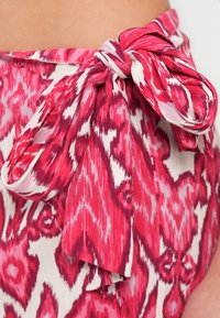 Ύφασμα με λουλουδάτο μοτίβο σε αποχρώσεις του ροζ και του λευκού, με λεπτομέρεια δεμένου κόμπου στη μέση και ρέουσα υφή.