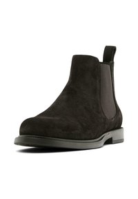 Stivaletto Chelsea in suede marrone scuro con pannello elastico ai lati e linguetta su una suola nera bassa.