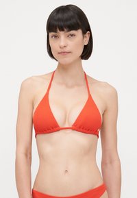 Rode geribbelde bikini-top met een driehoekig ontwerp, dunne bandjes en een strik in het midden. Zachte textuur met een minimalistische stijl.