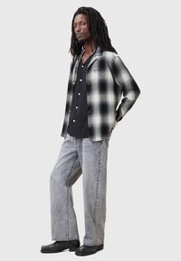 Camisa de cuadros en blanco y negro con botones, superpuesta a una camiseta negra, combinada con jeans de pierna ancha gris claro y zapatos negros.