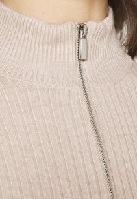 Light pink ribbed sweater with a high collar and a metal zipper closure in the front. The fabric has a smooth texture and snug fit.