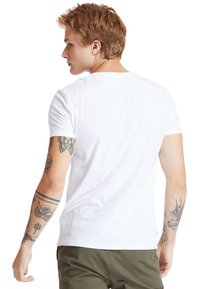Vit bomull t-shirt med korta ärmar, rund halsringning och regular fit. Har synliga tatueringar på armen och en enkel design på baksidan.