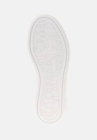 Sole di sneaker in gomma bianca con il nome del marchio "GUESS" impresso in un motivo ripetuto e un design curvo con una finitura testurizzata.