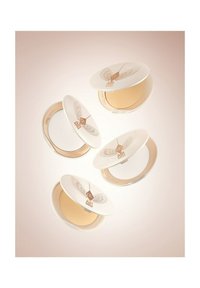 Four white compacts with gold accents and wing designs open to reveal a beige powder inside. They are arranged in a floating formation.