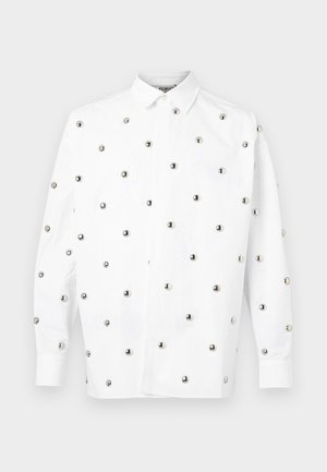 Camicia bianca a maniche lunghe con rivetti di metallo argentato disposti in un motivo sparso, con colletto a punta e chiusura frontale con bottoni.