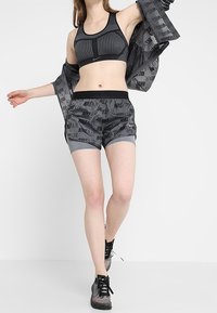 Soutien-gorge de sport noir et gris avec des rayures verticales, associé à un short gris arborant le logo "NIKE AIR", et des chaussures de sport noires.