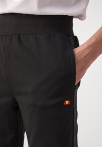 Zwarte sportbroek met een gestructureerde tailleband, zijzakken, een klein meerkleurig logo op het linkerbeen en patroonaccenten aan de zijkant.