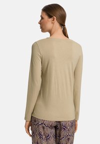 Camisa beige de manga larga con cuello redondo, textura suave y corte ajustado, combinada con pantalones morados estampados con motivos de hojas.