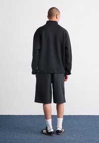 Black fleece sweatshirt with a high collar, paired with matching shorts. Simple design, relaxed fit, and styled with white socks and black sneakers.