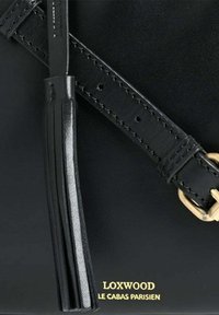 Sac en cuir noir avec une bandoulière réglable, boucle en or, pompon en cuir et texte doré "LOXWOOD LE CABAS PARISIEN" sur une surface lisse.