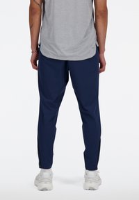 Mannen navy broek met een relaxte pasvorm en ritsdetails bij de enkels, gemaakt van lichtgewicht stof, gecombineerd met een grijs shirt.