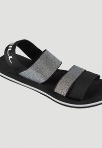 Mustat sandaalit, joissa on kaksi leveää remmiä; toinen on teksturoitua harmaata kangasta, ja toinen on sileää mustaa. Vastaava valkoinen pohja mustalla reunalla.