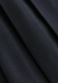 Schwarzer Stoff mit einer glatten Textur, der diagonale Rippmuster und einen subtilen Schimmer aufweist, in mehreren Lagen gefaltet.
