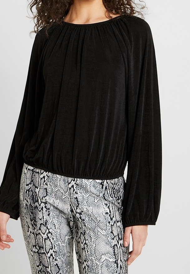 Czarna bluzka z długim rękawem, z marszczonym dekoltem i zwężanym dołem, w połączeniu z szarymi spodniami w wężowy wzór o gładkiej teksturze.
