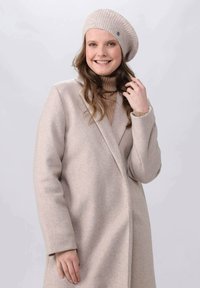 Beige wool coat with a double-breasted design and notched collar, worn over a beige turtleneck. Complemented by a matching ribbed beret.