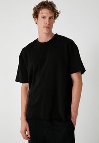 Sort kortærmet t-shirt lavet af bomuld, med rund hals og rå kanter, i en afslappet pasform uden synlige grafik.