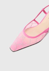 Zapato de slingback rosa con puntera cuadrada, parte superior transparente con adornos de cuentas en un patrón en espiral y suela negra plana.