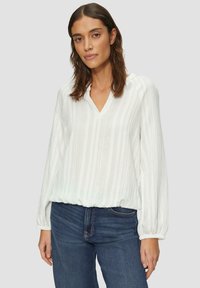 Witte blouse met lange mouwen, voorzien van een gestructureerd gestreept ontwerp, V-hals en elastische zoom, gecombineerd met donkerblauwe jeans.