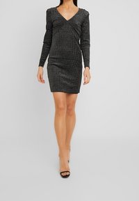 Svart långärmad klänning med djup V-ringning, med ett strukturerat mönster av små vita prickar, figursydd silhuett och knälång fåll.