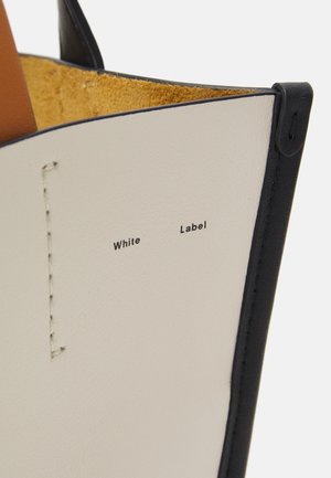 Nærbillede af hvidt læderobjekt med sort kant, gul ruskind indvendigt og teksten "White Label" trykt på overfladen.