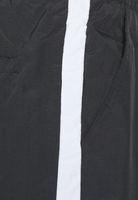 Černá tkanina s mačkanou strukturou, se svislým bílým pruhem. Obsahuje kapsu na levé straně, viditelné šití.