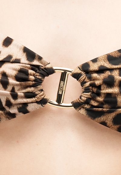 Ύφασμα με μοτίβο λεοπάρ γύρω από ένα χρυσό οβάλ δαχτυλίδι με εγχάραξη λογότυπου, φορεμένο ως κομψό ρούχο αξεσουάρ.