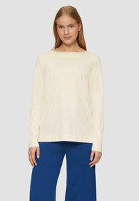 Langsleeve top met een bootnek, gemaakt van licht crèmekleurige stof. Heeft een relaxte pasvorm met rechte zoom en wordt gecombineerd met blauw wijde broek.