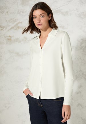 Langarm-Hemd mit Knöpfen aus off-white Stoff mit Kragen, im lässigen Schnitt und mit glatter Textur, kombiniert mit dunkelblauer Jeans.