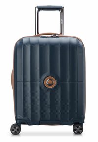 Valigia rigida di colore blu scuro con superficie testurizzata, dettagli in beige, manico retrattile e quattro ruote per la mobilità. Dettaglio con logo circolare.