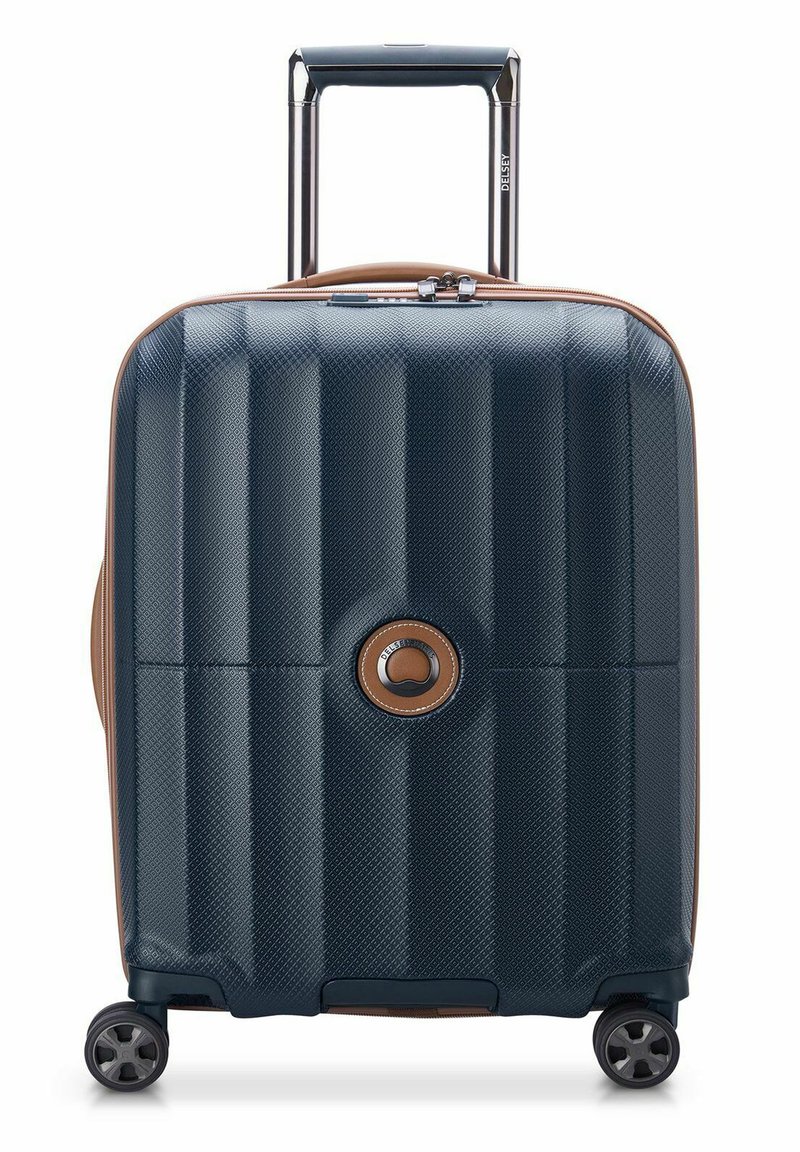 Valigia rigida di colore blu scuro con superficie testurizzata, dettagli in beige, manico retrattile e quattro ruote per la mobilità. Dettaglio con logo circolare.