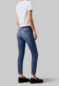 Smala blå jeans i denim, med medelhög midja, bakfickor och en ren finish. Kombineras med en kortärmad vit t-shirt.