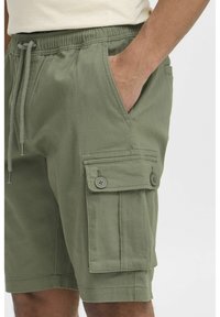 Pantalonii scurți cargo din bumbac verde au un talie elastică cu șnur, buzunare laterale și un buzunar cargo cu închidere buton.