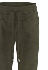 Olijf groene joggers gemaakt van zachte stof hebben een elastische tailleband met trekkoord en zilveren metalen accenten. Soepele textuur, minimalistisch ontwerp.
