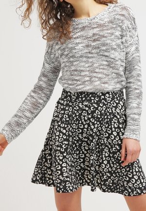 Femme portant un pull en maille gris et blanc et une jupe noire évasée avec un motif léopard blanc.