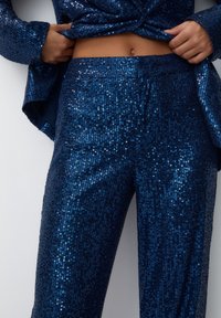 Dwuczęściowy zestaw ozdobiony cekinami w głębokim granatowym kolorze, składający się z dopasowanej bluzki i szerokich spodni, podkreślający błyszczącą teksturę i elegancki design.