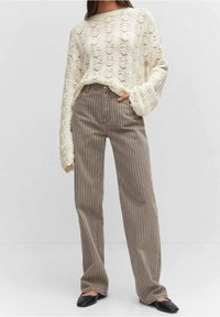 Pull crème en tricot avec un motif en losanges texturé, associé à un pantalon à rayures marron taille haute et des chaussures plates noires.