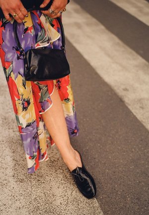 Scarpe in pelle nera con dettaglio a fiocco, indossate con un abito maxi a fantasia floreale in colori vivaci, che mostra fiori audaci e un tessuto fluido.