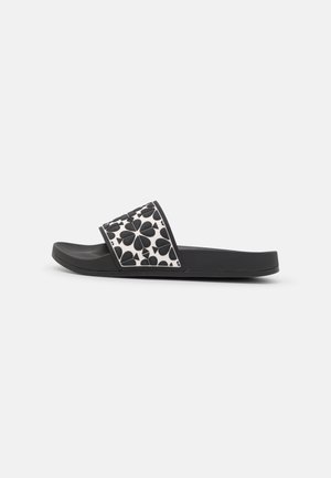 Sandale à enfiler noire avec une bride blanche présentant un motif de cœur et de trèfle noir, semelle plate et design à bout ouvert.